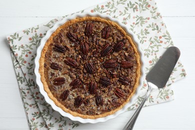 Delicious pecan pie in baking dish and cake server on white wooden table, flat lay