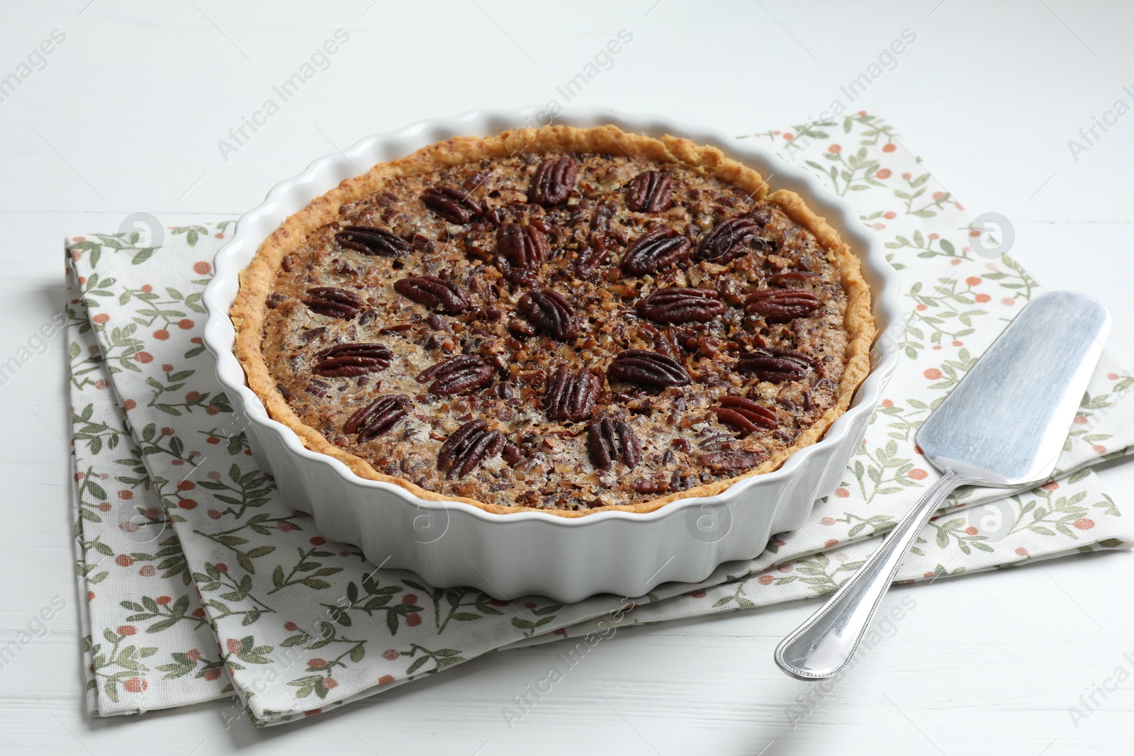 Photo of Delicious pecan pie in baking dish and cake server on white wooden table