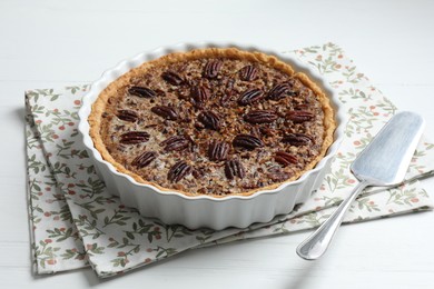 Photo of Delicious pecan pie in baking dish and cake server on white wooden table