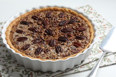 Delicious pecan pie in baking dish and cake server on white table, closeup