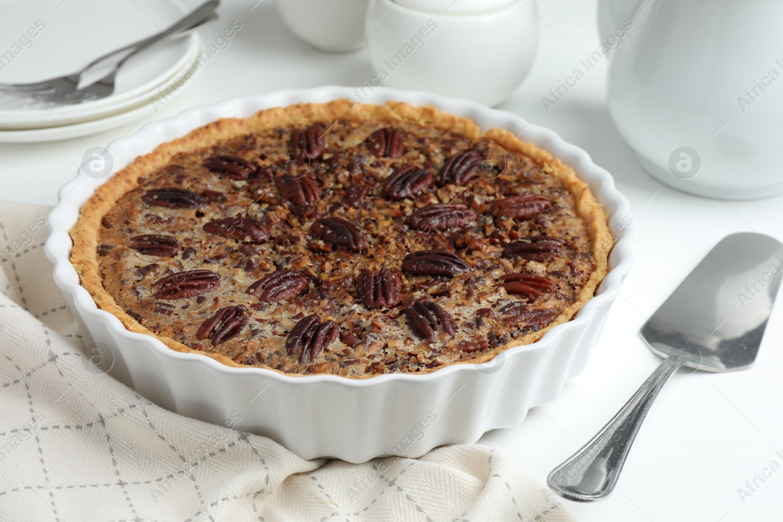 Photo of Delicious pecan pie in baking dish and cake server on white table