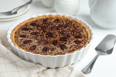 Delicious pecan pie in baking dish and cake server on white table