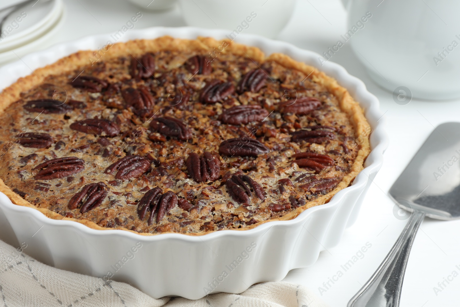 Photo of Delicious pecan pie in baking dish and cake server on white table, closeup