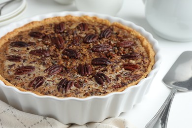 Delicious pecan pie in baking dish and cake server on white table, closeup