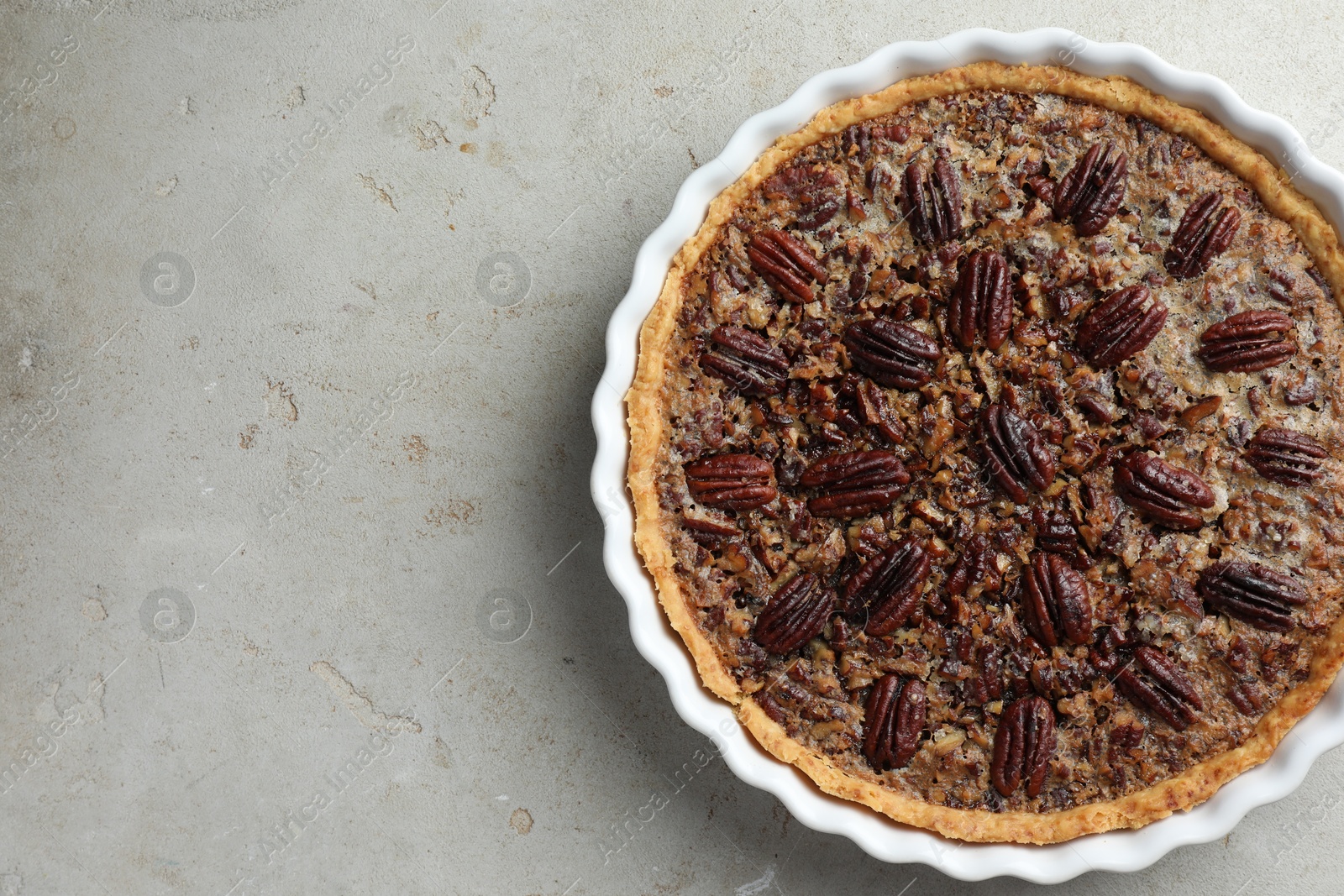 Photo of Delicious pecan pie in baking dish on gray textured table, top view. Space for text