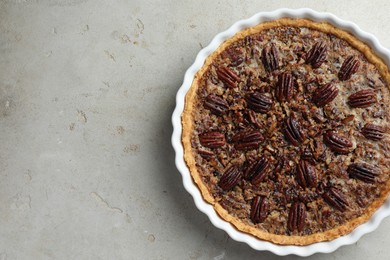 Delicious pecan pie in baking dish on gray textured table, top view. Space for text