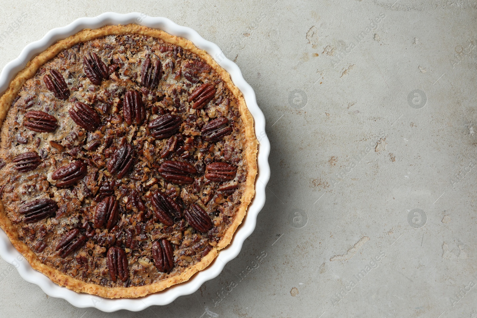 Photo of Delicious pecan pie in baking dish on gray textured table, top view. Space for text