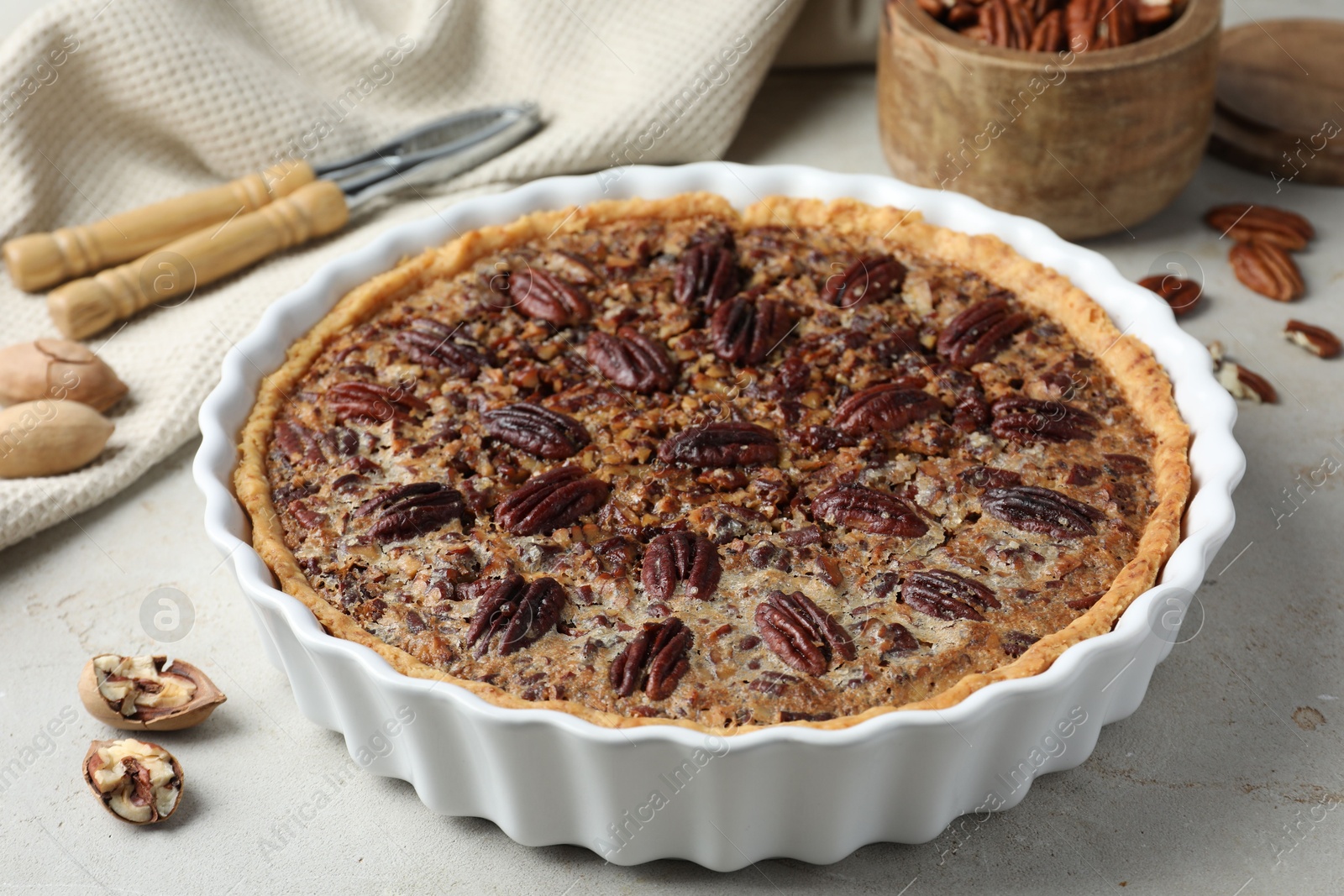 Photo of Delicious pecan pie in baking dish and fresh nuts on gray textured table, closeup