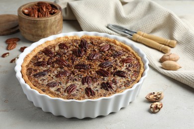 Photo of Delicious pecan pie in baking dish and fresh nuts on gray textured table, closeup