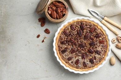 Photo of Delicious pecan pie in baking dish, nutcracker and fresh nuts on gray textured table, flat lay. Space for text