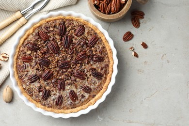 Photo of Delicious pecan pie in baking dish, nutcracker and fresh nuts on gray textured table, flat lay. Space for text