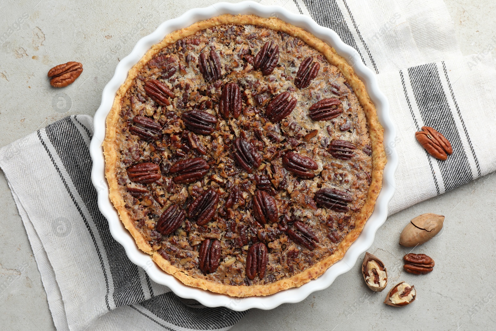 Photo of Delicious pecan pie in baking dish and fresh nuts on gray textured table, top view