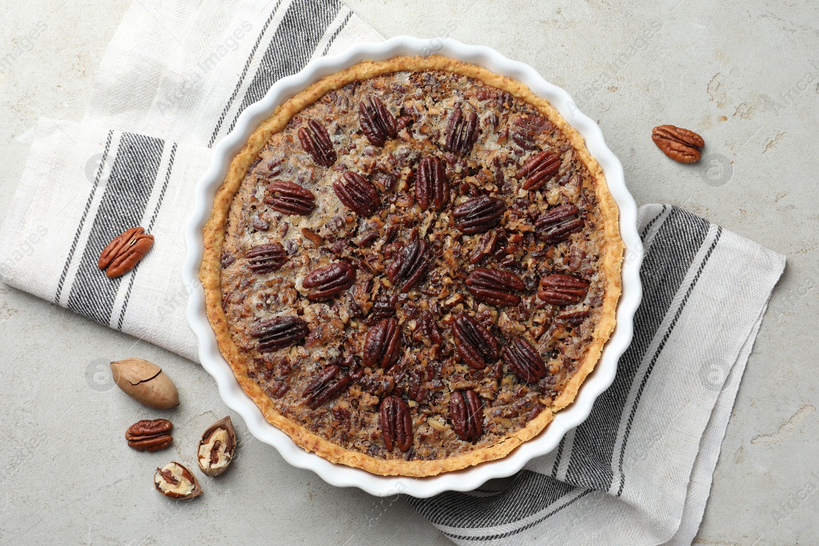 Photo of Delicious pecan pie in baking dish and fresh nuts on gray textured table, top view