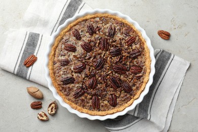 Photo of Delicious pecan pie in baking dish and fresh nuts on gray textured table, top view