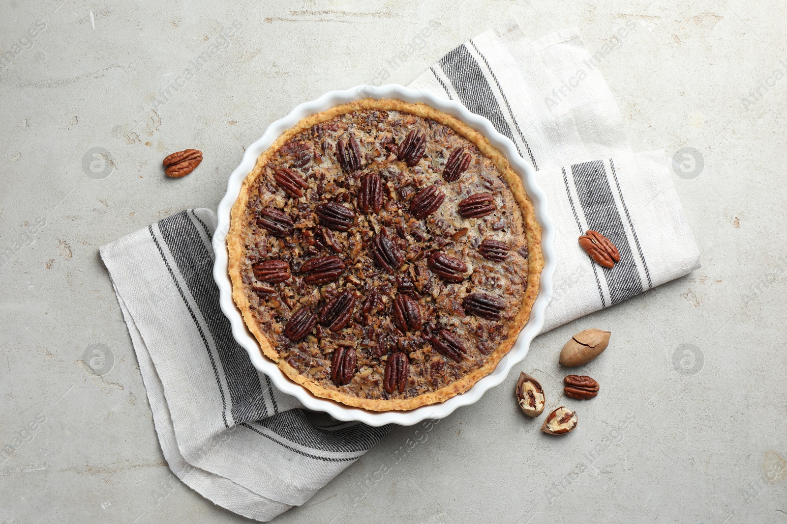 Photo of Delicious pecan pie in baking dish and fresh nuts on gray textured table, top view