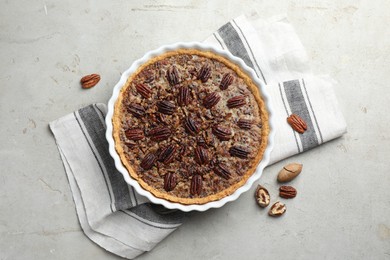 Photo of Delicious pecan pie in baking dish and fresh nuts on gray textured table, top view