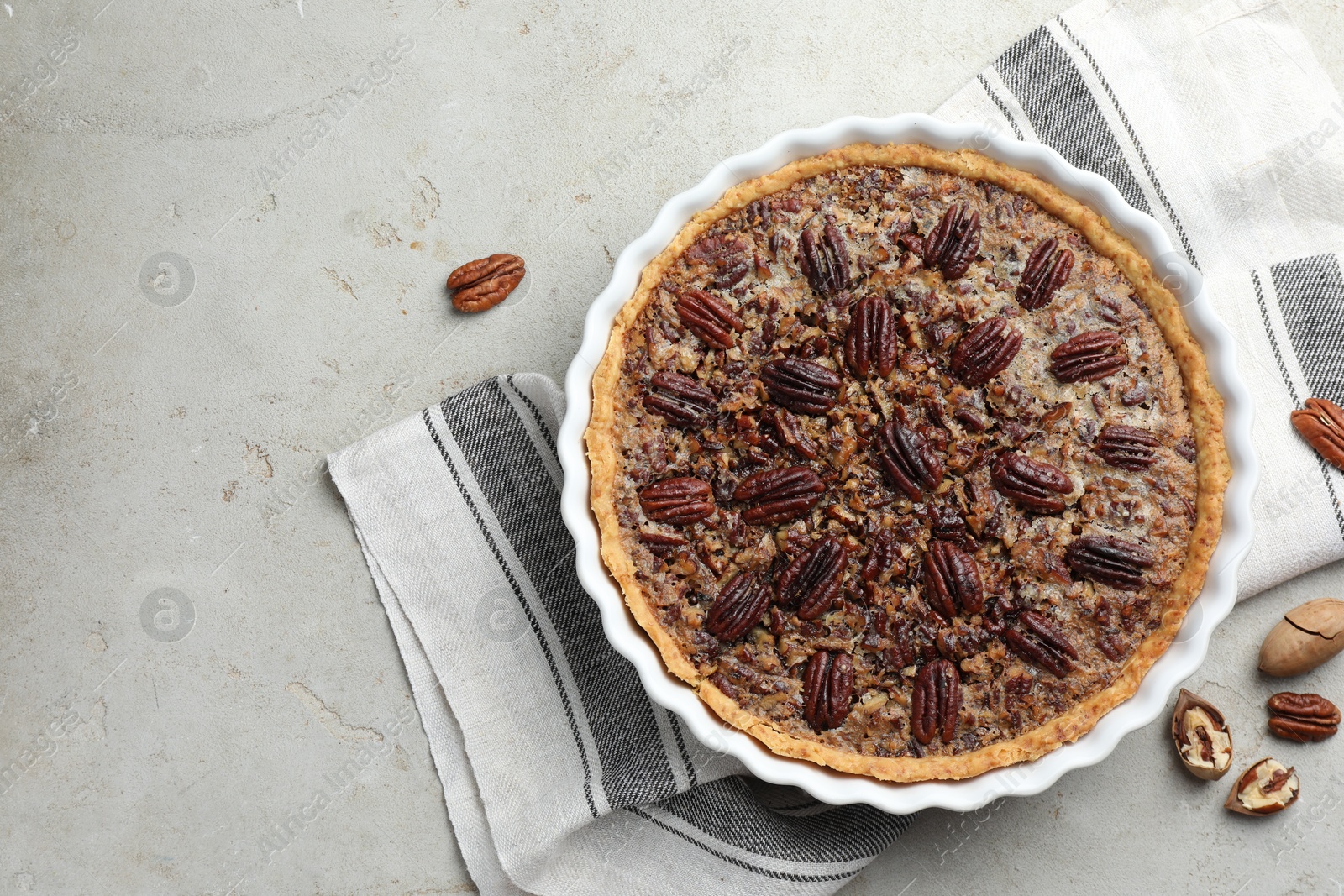 Photo of Delicious pecan pie in baking dish and fresh nuts on gray table, top view. Space for text