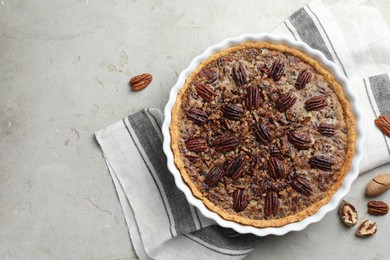 Delicious pecan pie in baking dish and fresh nuts on gray table, top view. Space for text