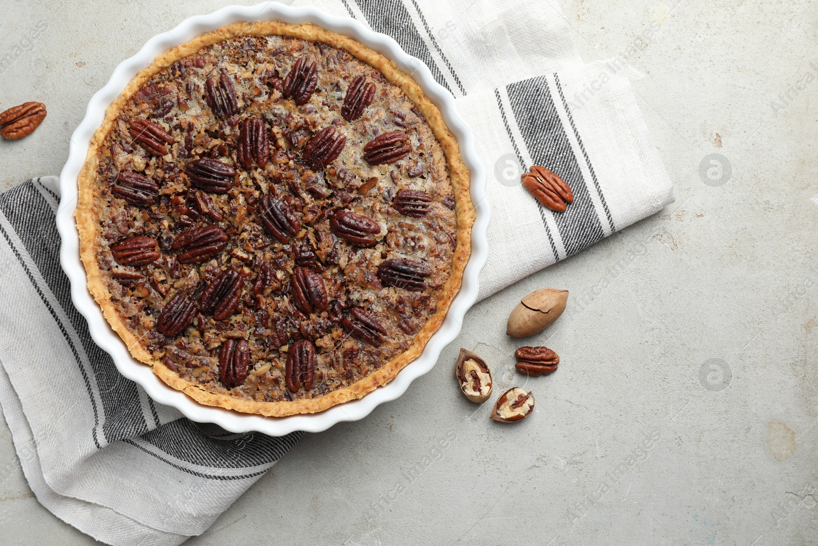 Photo of Delicious pecan pie in baking dish and fresh nuts on gray textured table, top view