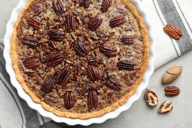 Photo of Delicious pecan pie in baking dish and fresh nuts on gray textured table, top view