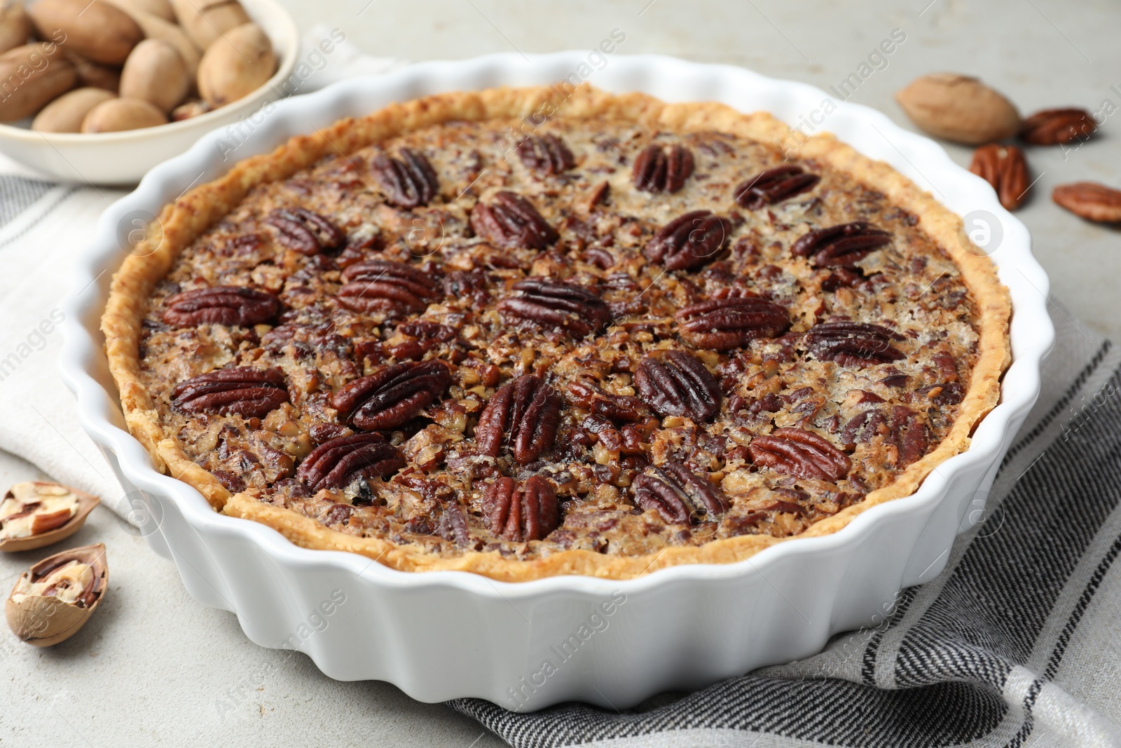 Photo of Delicious pecan pie in baking dish and fresh nuts on gray textured table, closeup