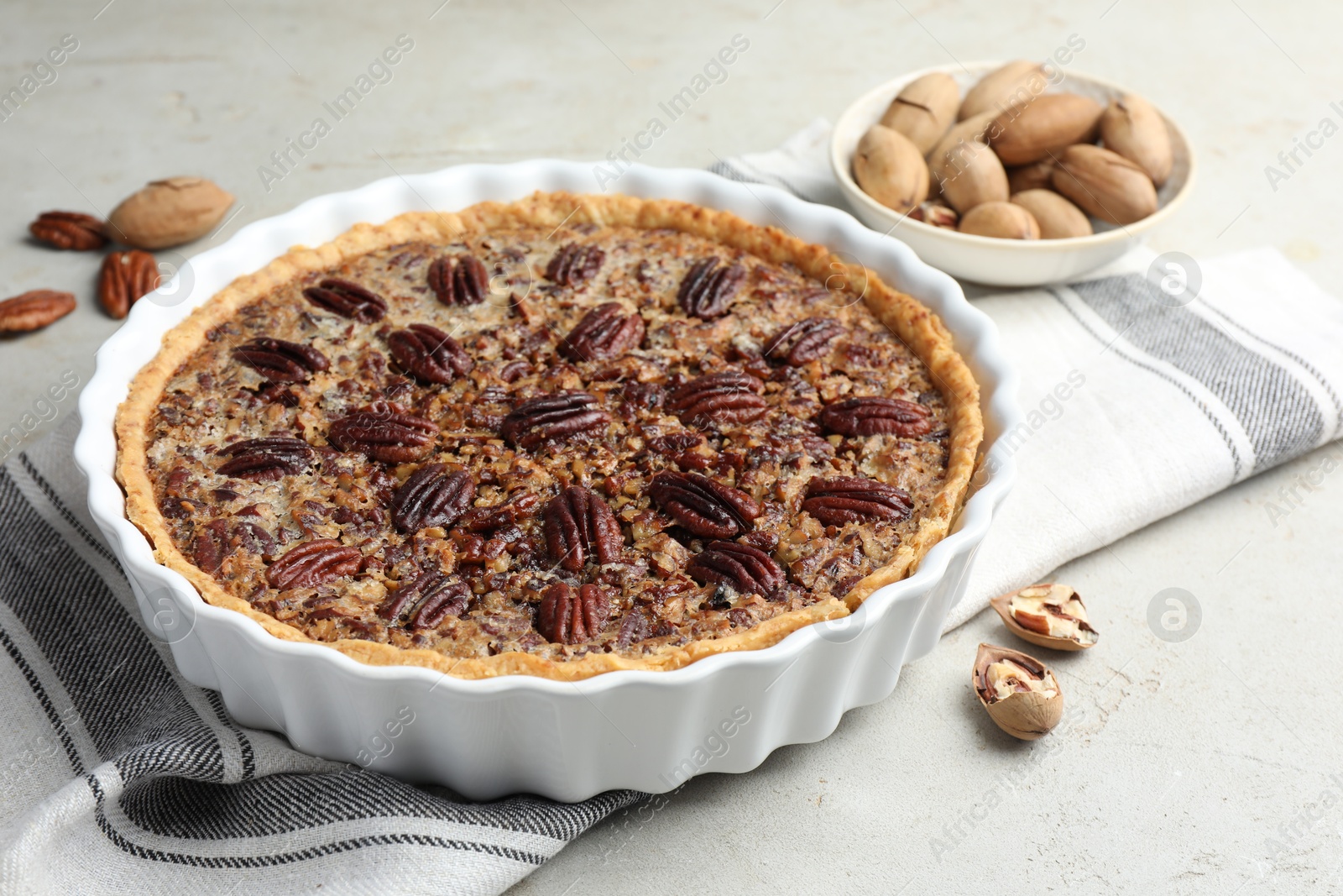 Photo of Delicious pecan pie in baking dish and fresh nuts on gray textured table, closeup