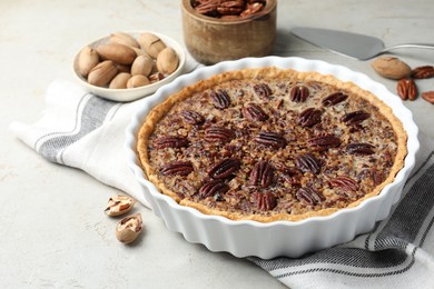 Delicious pecan pie in baking dish and fresh nuts on gray textured table, closeup