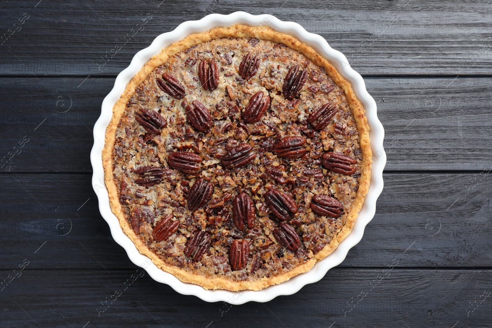 Photo of Delicious pecan pie in baking dish on dark wooden table, top view