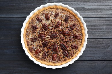 Photo of Delicious pecan pie in baking dish on dark wooden table, top view