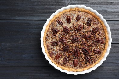 Photo of Delicious pecan pie in baking dish on dark wooden table, top view. Space for text