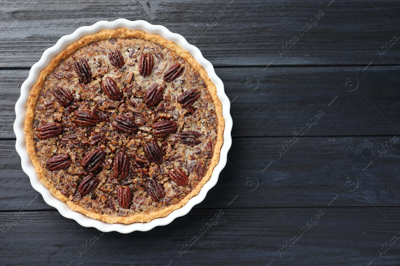 Photo of Delicious pecan pie in baking dish on dark wooden table, top view. Space for text