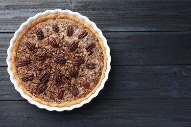 Photo of Delicious pecan pie in baking dish on dark wooden table, top view. Space for text