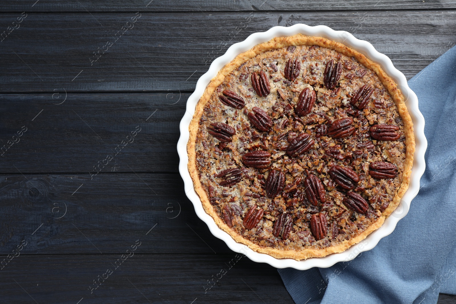 Photo of Delicious pecan pie in baking dish on dark wooden table, top view. Space for text