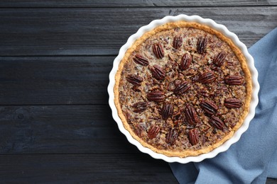 Photo of Delicious pecan pie in baking dish on dark wooden table, top view. Space for text