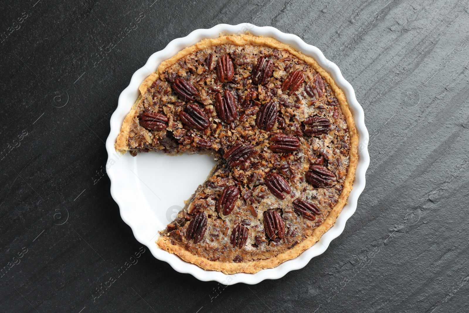 Photo of Delicious pecan pie in baking dish on dark gray textured table, top view