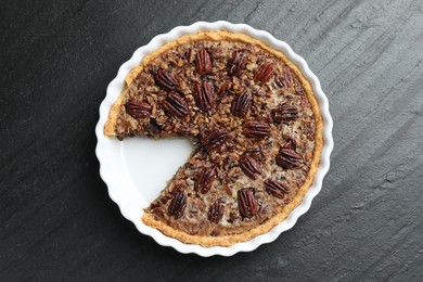 Photo of Delicious pecan pie in baking dish on dark gray textured table, top view