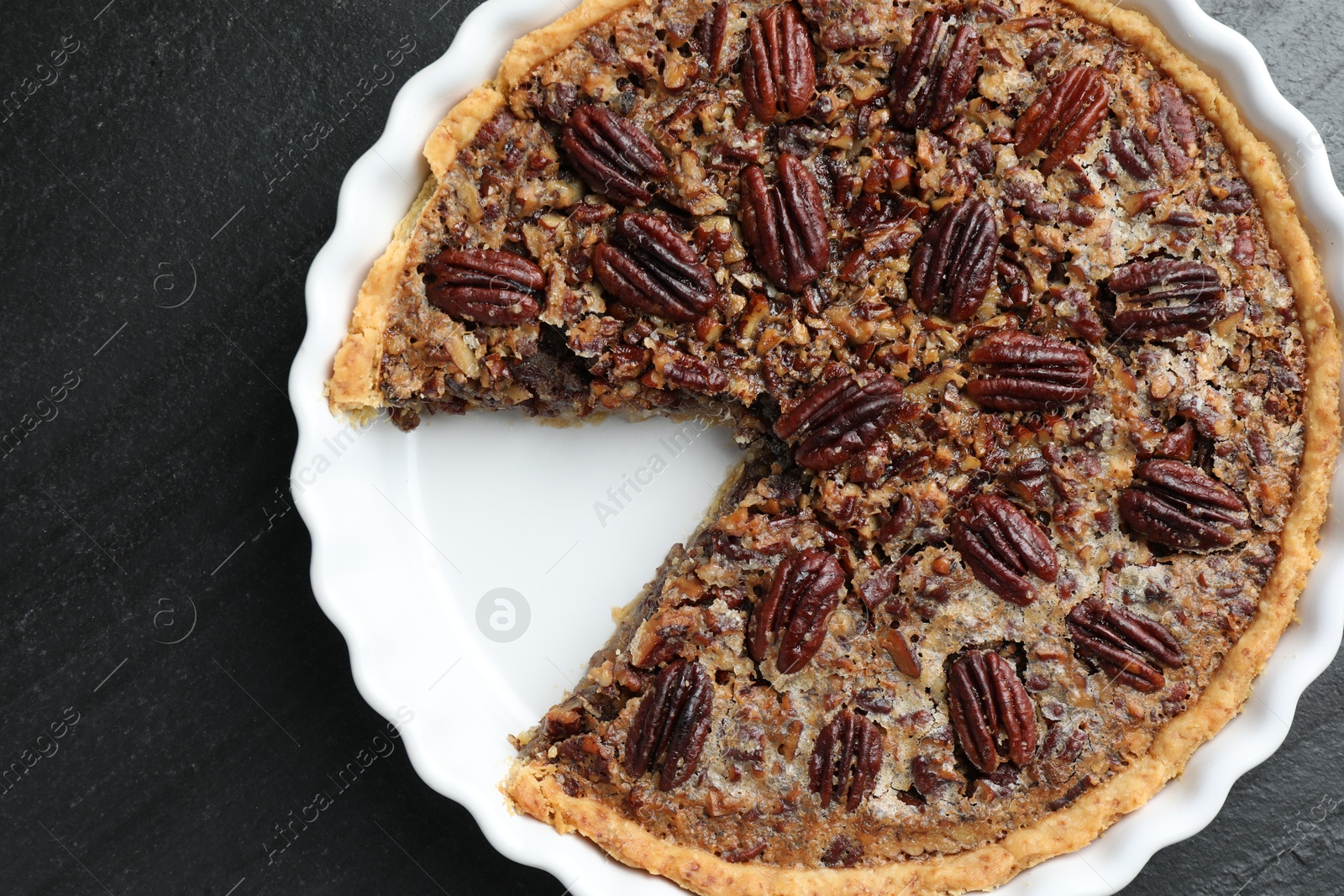 Photo of Delicious pecan pie in baking dish on dark gray textured table, top view