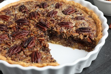 Delicious pecan pie in baking dish on dark gray textured table, closeup