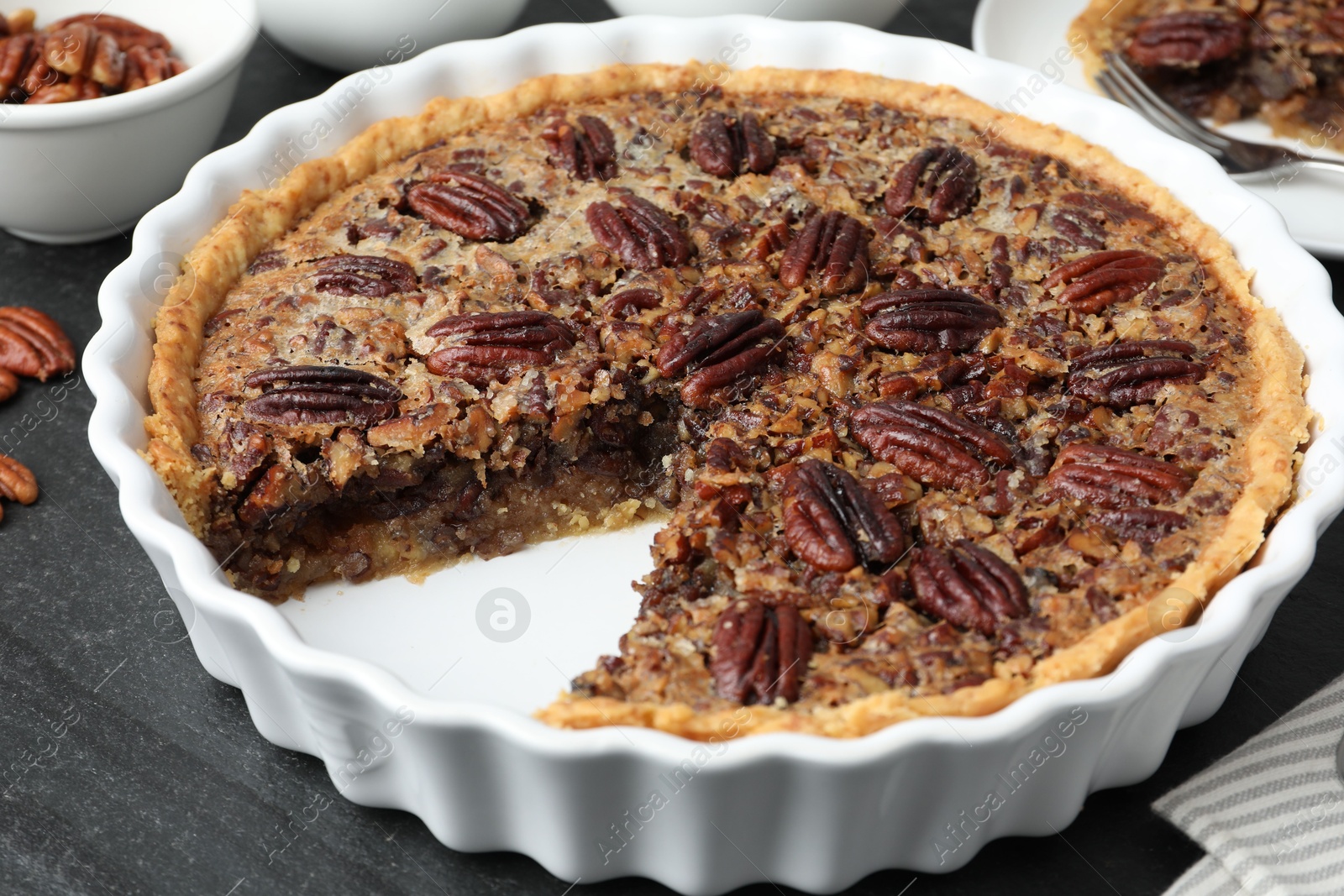 Photo of Delicious pecan pie in baking dish on dark gray textured table, closeup