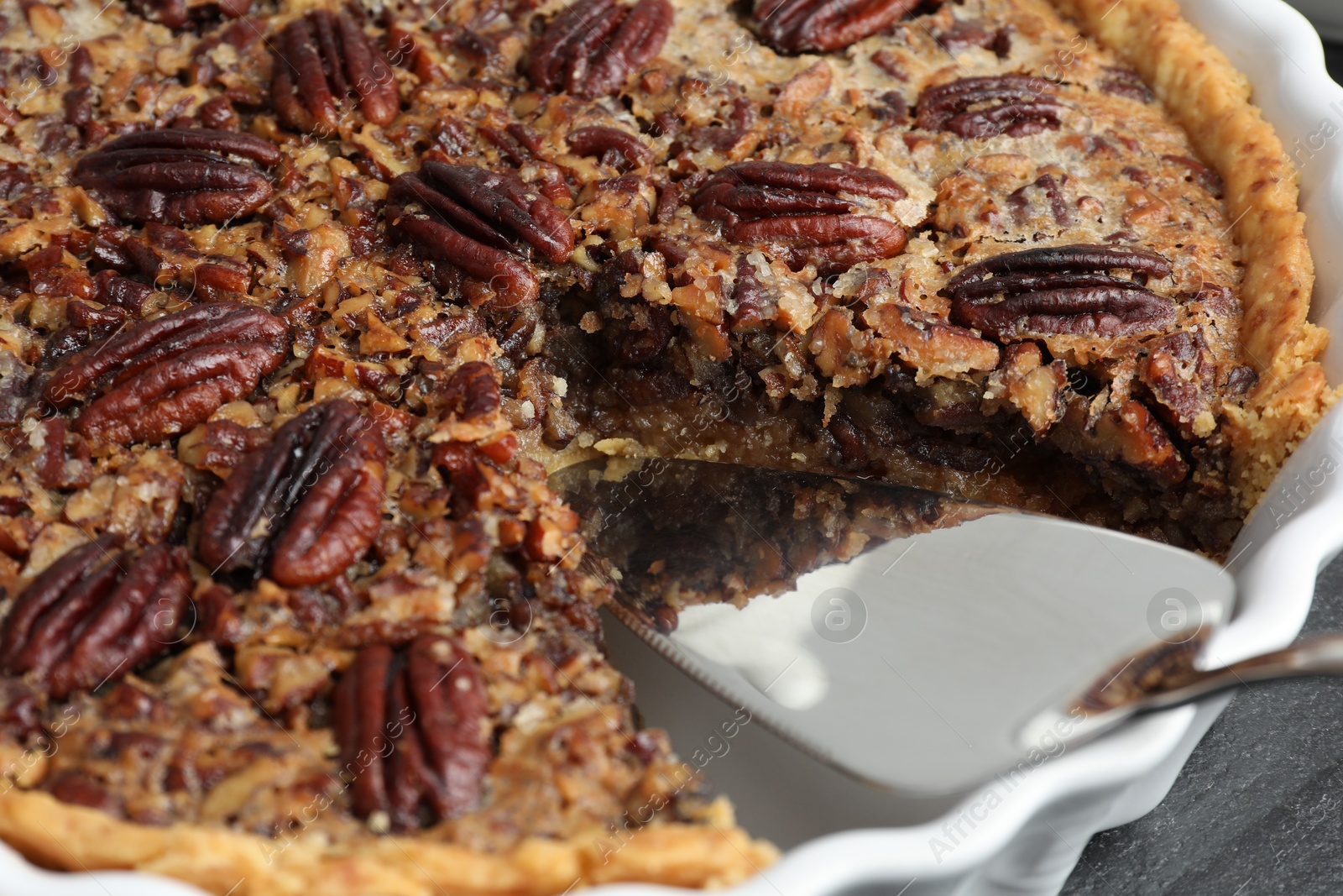 Photo of Delicious pecan pie in baking dish and cake server on table, closeup