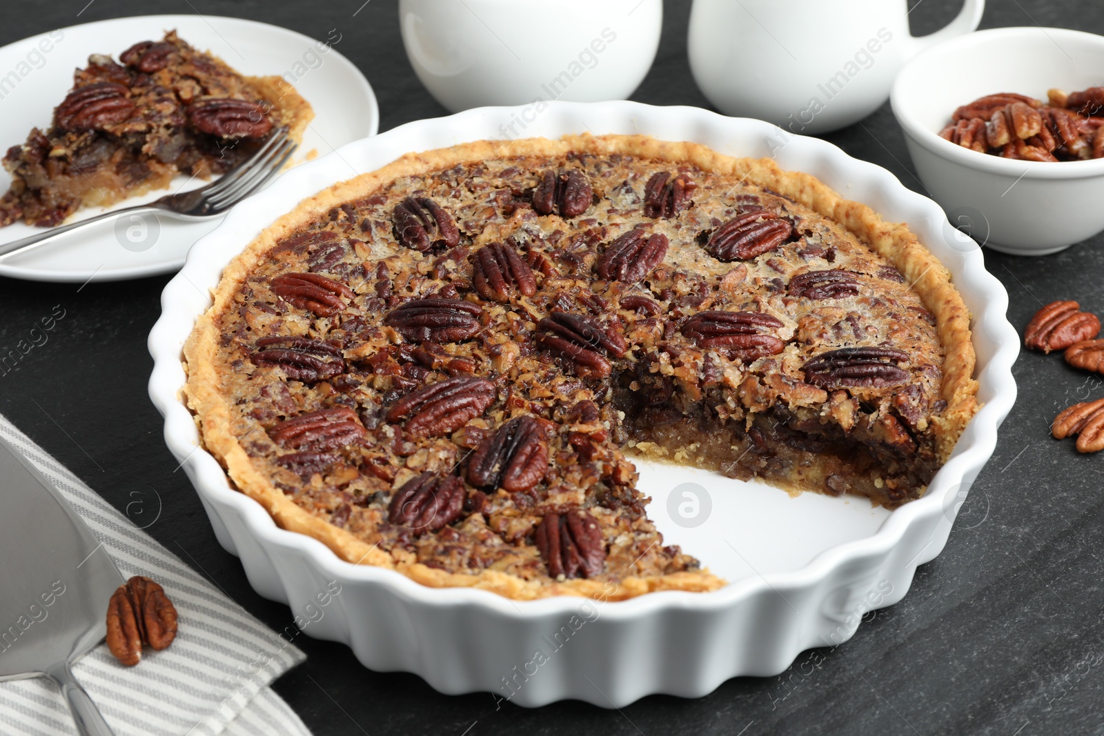 Photo of Delicious pecan pie in baking dish on dark gray textured table, closeup