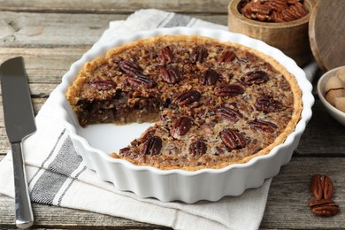 Photo of Delicious pecan pie in baking dish and knife on wooden table, closeup