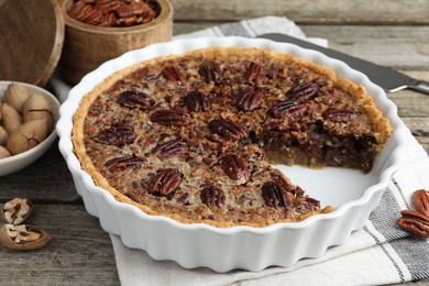 Delicious pecan pie in baking dish and fresh nuts on wooden table, closeup