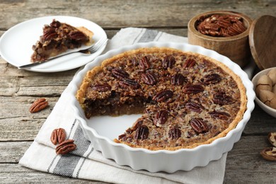 Delicious pecan pie in baking dish and fresh nuts on wooden table, closeup