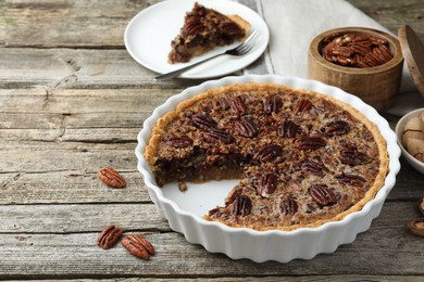 Photo of Delicious pecan pie in baking dish and fresh nuts on wooden table