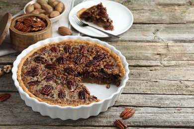 Delicious pecan pie in baking dish and fresh nuts on wooden table. Space for text