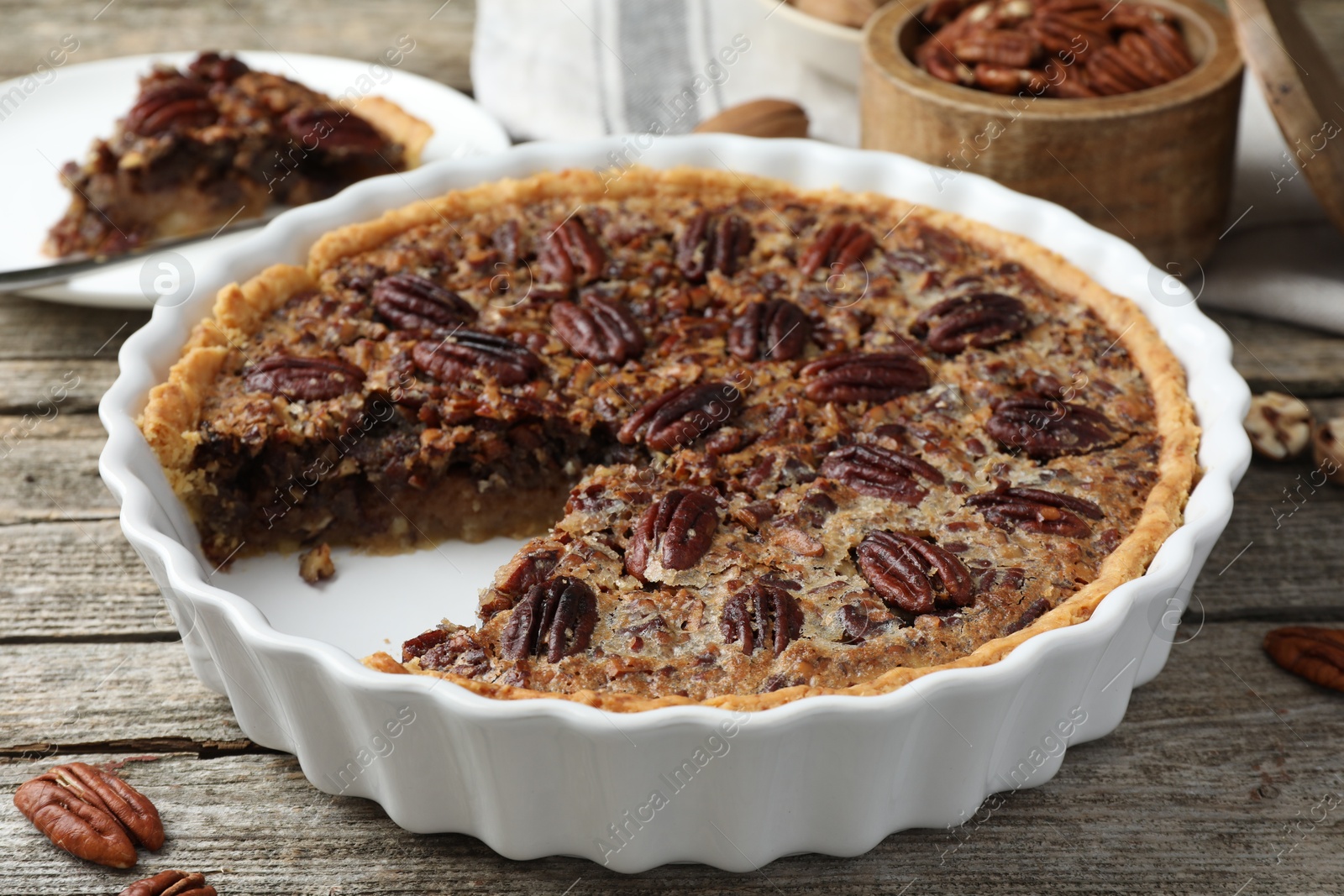 Photo of Delicious pecan pie in baking dish on wooden table, closeup