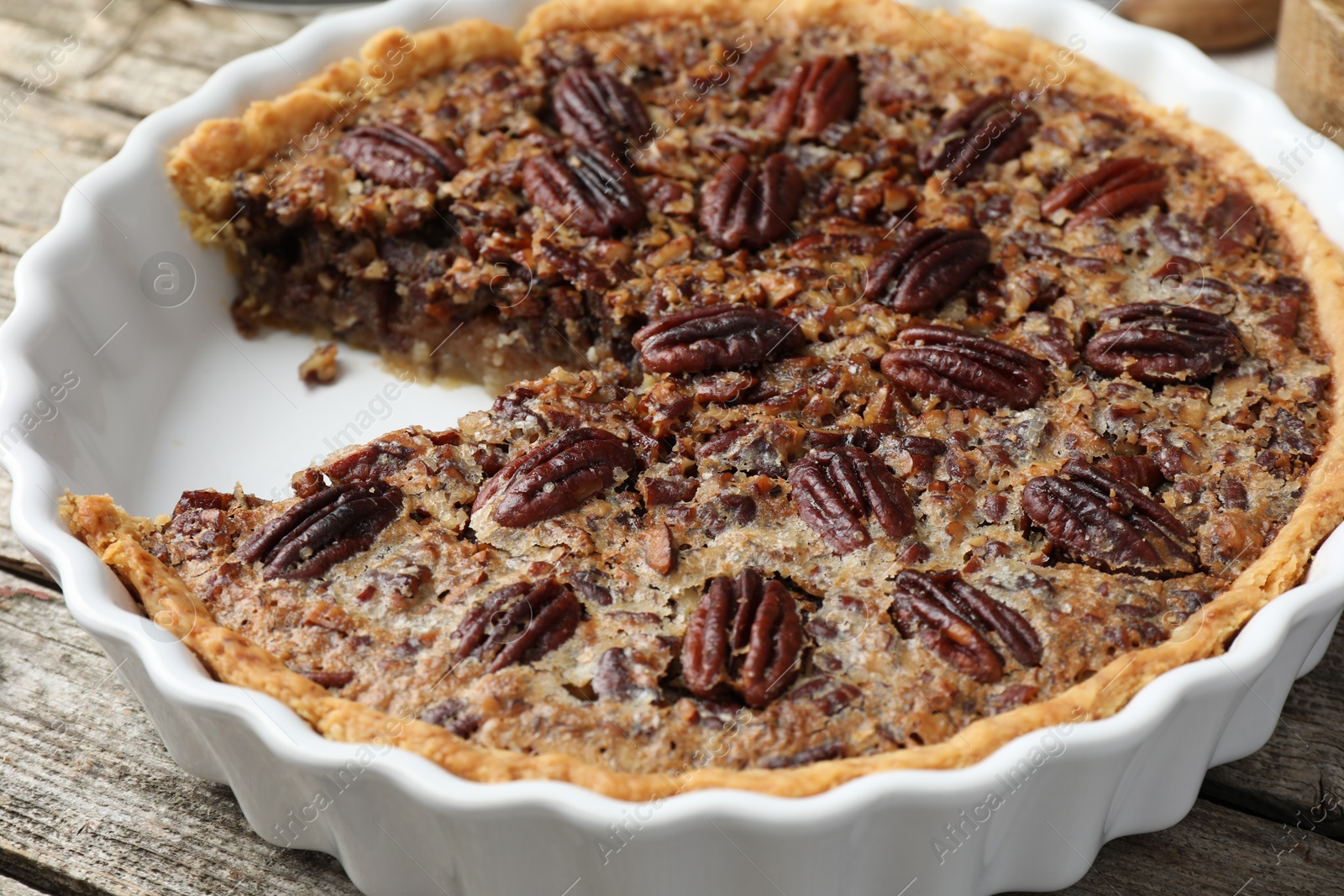 Photo of Delicious pecan pie in baking dish on wooden table, closeup