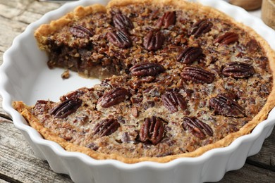 Delicious pecan pie in baking dish on wooden table, closeup