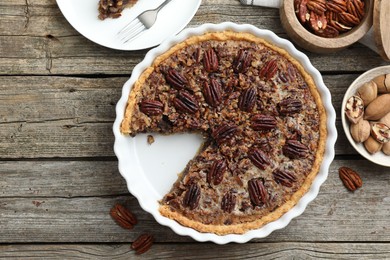 Photo of Delicious pecan pie in baking dish and fresh nuts on wooden table, flat lay